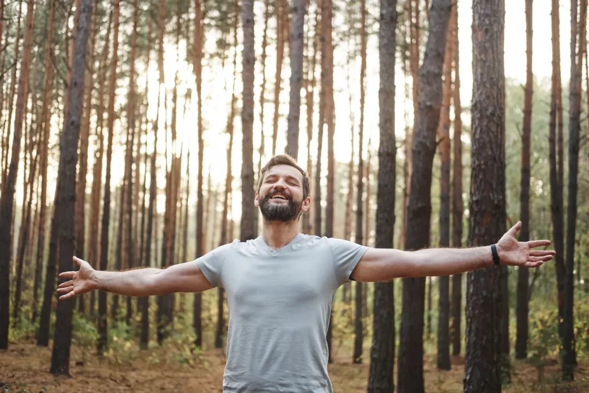 Man smiling in the woods with his arms out expressing happiness